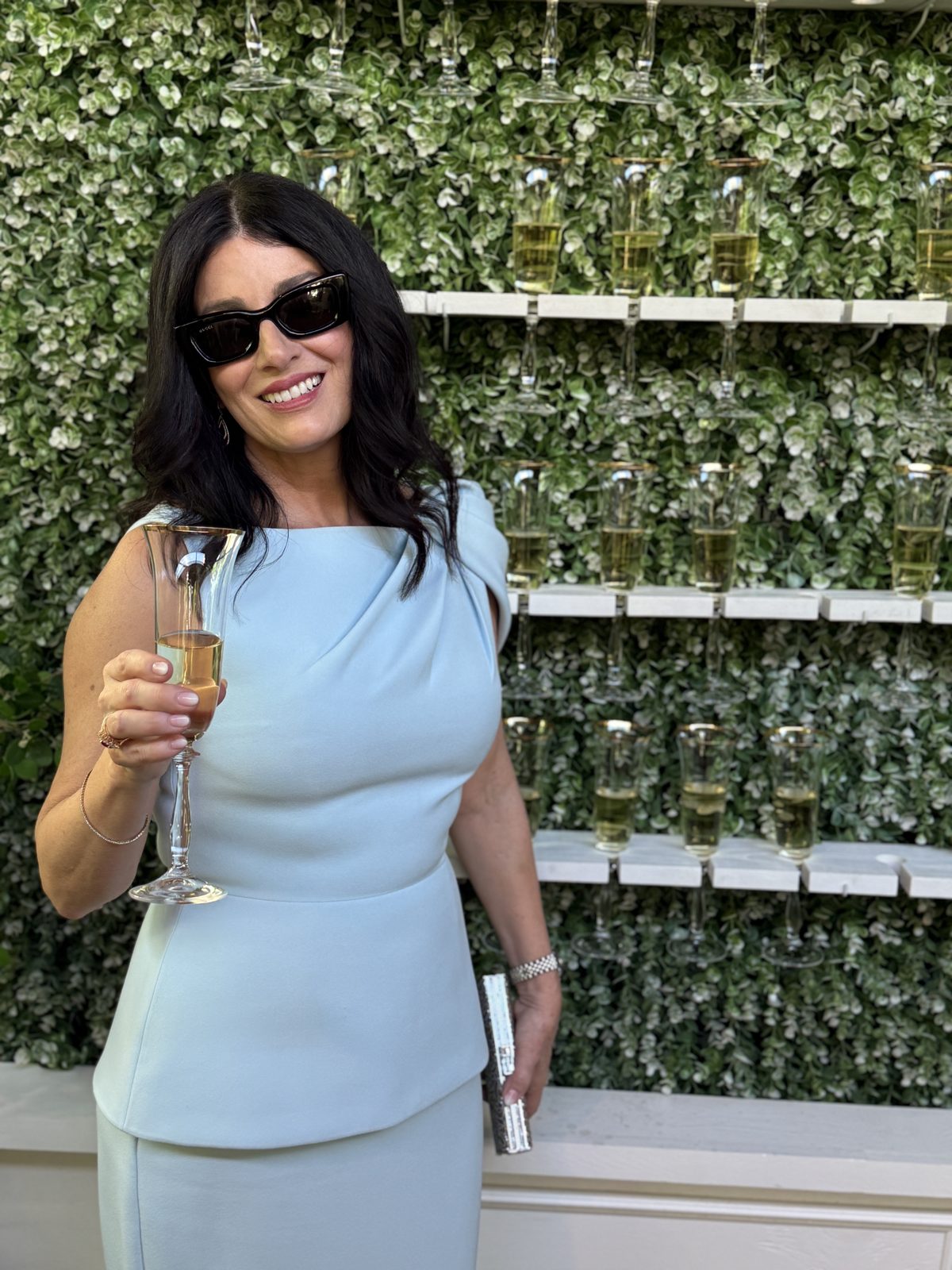 Denise Jonas raising a champagne glass in front of an ivy wall