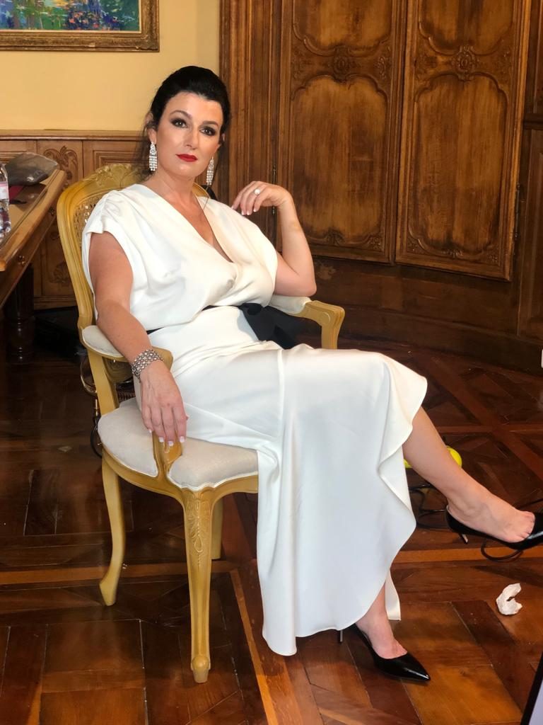 Denise Jonas in a white dress seated in an antique chair